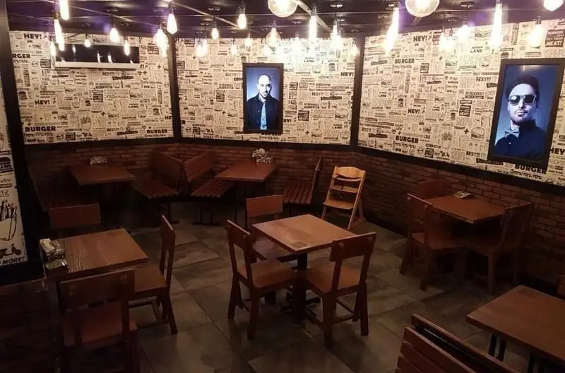 فضای داخلی جذاب رستوران برگرلند با دکوراسیون روزنامه‌ای دیواری و آجرهای قهوه‌ای، میز و صندلی‌های چوبی شیک و نورپردازی دلنشین.
