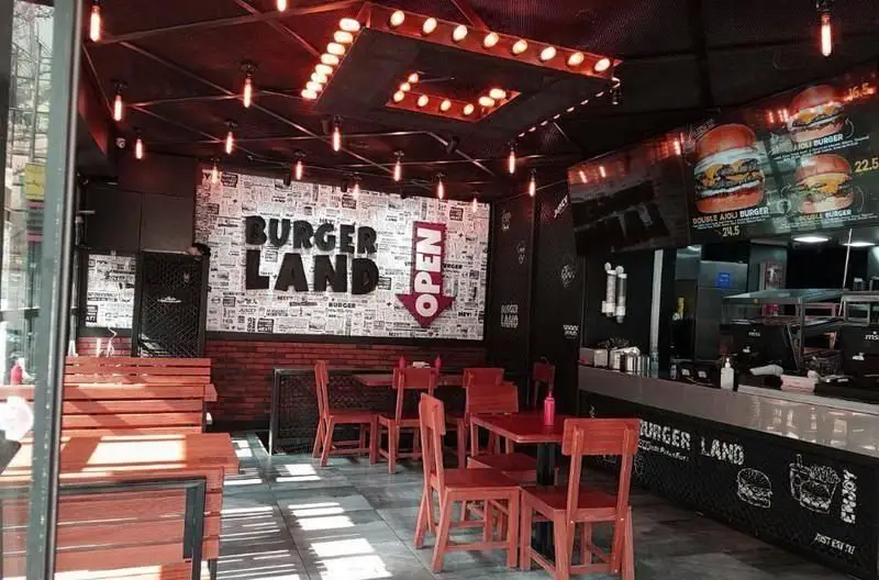 فضای داخلی رستوران برگرلند با دکوراسیون جذاب و مدرن، میز و صندلی چوبی، تابلوی برگرلند و منوی دیجیتال سفارش غذا.