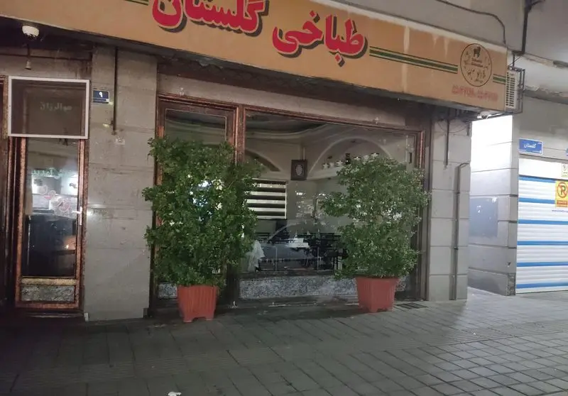 نمای خارجی طباخی گلستان، مرکز کله پاچه، در شب. تابلوی بزرگ و شیشه‌ای این رستوران با دو گلدان تزئینی دیده می‌شود.