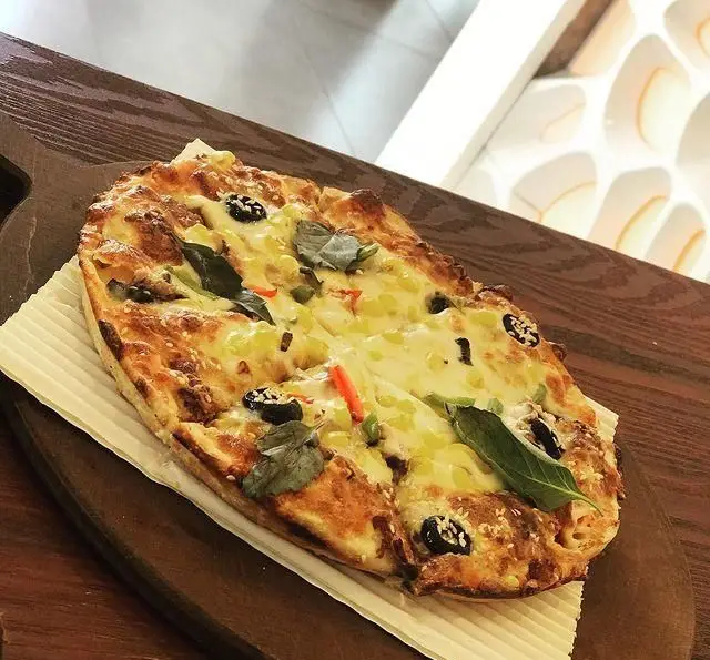 پیتزا بیضی شکل مخصوص و خوشمزه فست فود چهل سی با پنیر فراوان، زیتون سیاه و سبزیجات تازه، روی تخته چوبی شیک، آماده سفارش.