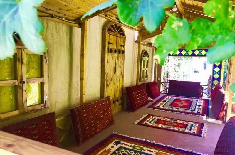 کافی شاپ سفره خانه سنتی طاها1، فضایی آرام و سنتی با سقف چوبی، درب و پنجره‌های قدیمی، قالیچه‌های اصیل و نشیمن‌های راحت با نمایی سرسبز