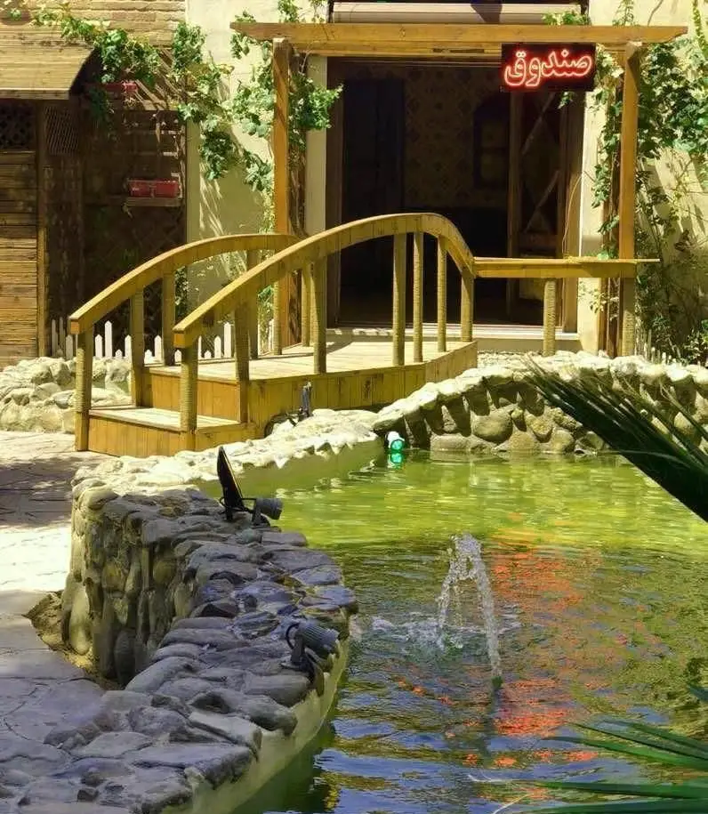 فضای دلنشین کافی شاپ سفره خانه سنتی طاها1 با پل چوبی، برکه آبنما و معماری سنتی. مکانی آرامش‌بخش برای مشتریان.