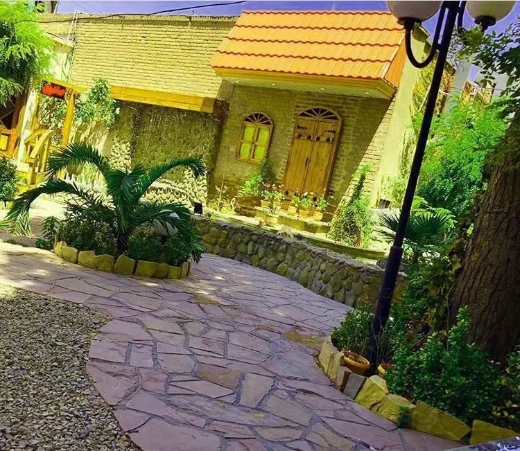 تصویری دلنشین از حیاط سرسبز و فضای باز کافی شاپ سفره خانه سنتی طاها1، شامل معماری سنتی بنا، مسیر سنگفرش و پوشش گیاهی زیبا.