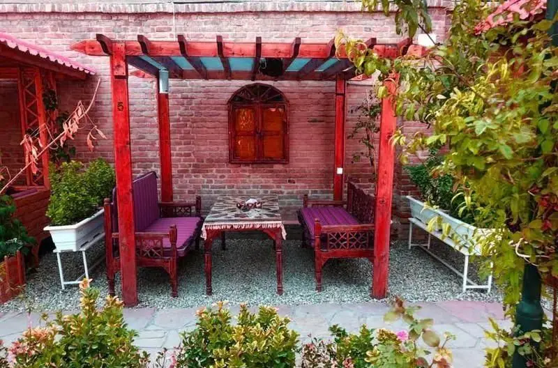 فضای باز و دنج کافی شاپ سفره خانه سنتی طاها1، شامل آلاچیق چوبی قرمز، نیمکت‌های بنفش و میز سنتی.