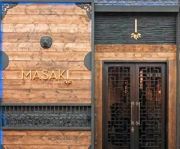 نمای بیرونی مدرن و جذاب رستوران آسیایی ماساکی، شامل پنل‌های چوبی، شیر سنگی، نماد لوتوس و درب‌های فلزی با طراحی هندسی.