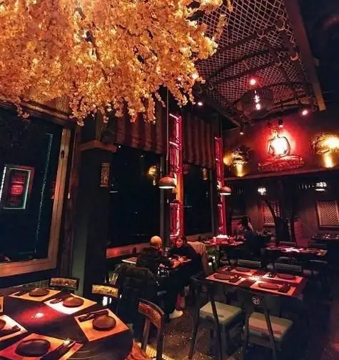 فضای داخلی رستوران آسیایی ماساکی: دکوراسیون شیک، نورپردازی گرم، سقف پوشیده از گل‌های زیبا، مجسمه بودا، میزهای آماده و مهمانان.