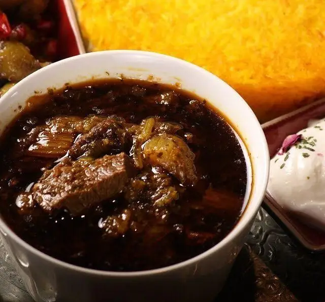 یک کاسه خورش فسنجان مجلسی کافه رستوران گردو با گوشت در سس غلیظ گردو و انار، در کنار پلو زعفرانی و ماست و خیار.