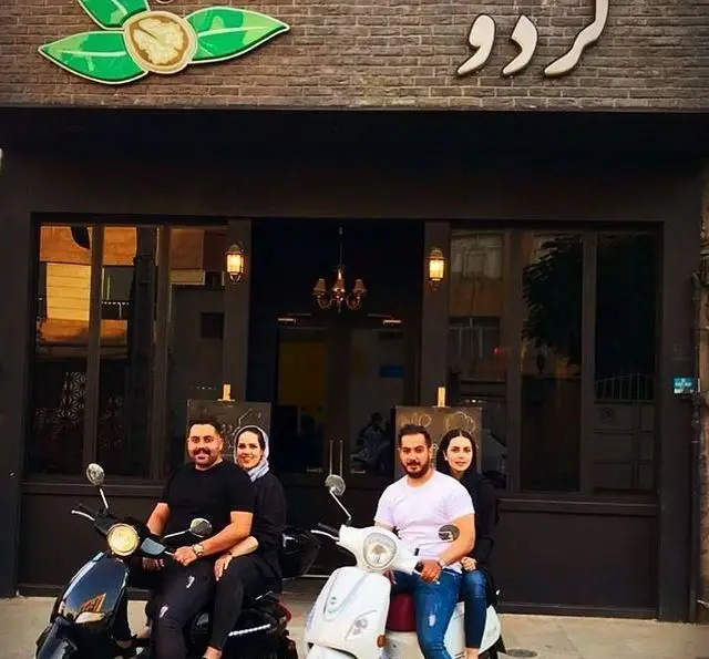 نمای بیرونی کافه رستوران گردو با چهار مشتری شاداب سوار بر دو اسکوتر جلوی ورودی شیک، همراه با لوگوی گردو.