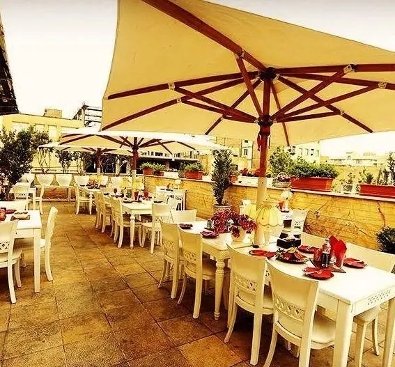 کافه رستوران گردو، فضایی دلنشین و دنج با چترهای آفتابگیر، میز و صندلی‌های سفید، مناسب برای صرف غذا در فضای باز.