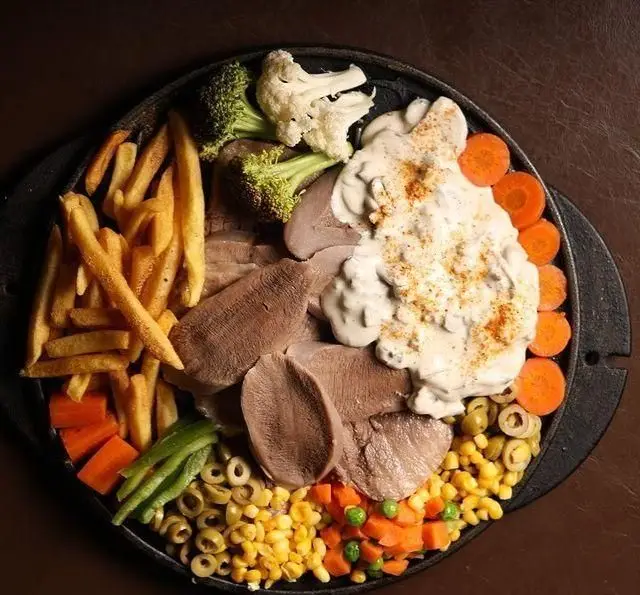 سینی داغ زبان با سیب زمینی سرخ کرده، سس قارچ، بروکلی، کلم، هویج، زیتون و ذرت در کافه رستوران گردو. یک غذای کامل.