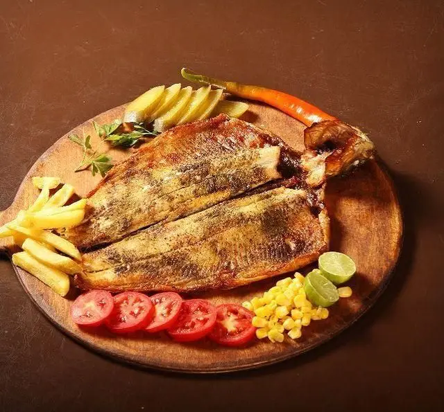 ماهی قزل آلا کبابی خوشمزه در کافه رستوران گردو همراه با سیب زمینی سرخ کرده، گوجه، ذرت و لیمو تازه، یک غذای دریایی عالی.