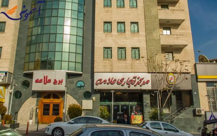 تصویر نمای بیرونی مجتمع تجاری علامه، ساختمانی بزرگ با معماری مدرن و شیشه، محلی عالی برای انواع فروشگاه‌ها و کسب‌وکارهای موفق.