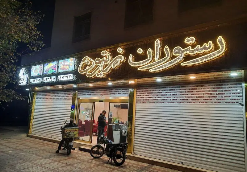 نمای بیرونی شبانه رستوران زیتون با تابلوی نئون روشن، آماده ارائه خدمات و تحویل غذا با حضور موتورهای پیک.