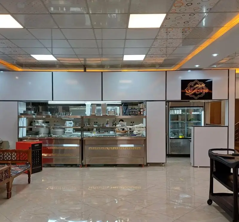 نمای داخلی رستوران سنتی منوچ با آشپزخانه صنعتی، تجهیزات پخت و پز، کانترهای استیل و سقف مدرن. محیطی تمیز و دلپذیر برای مشتریان.