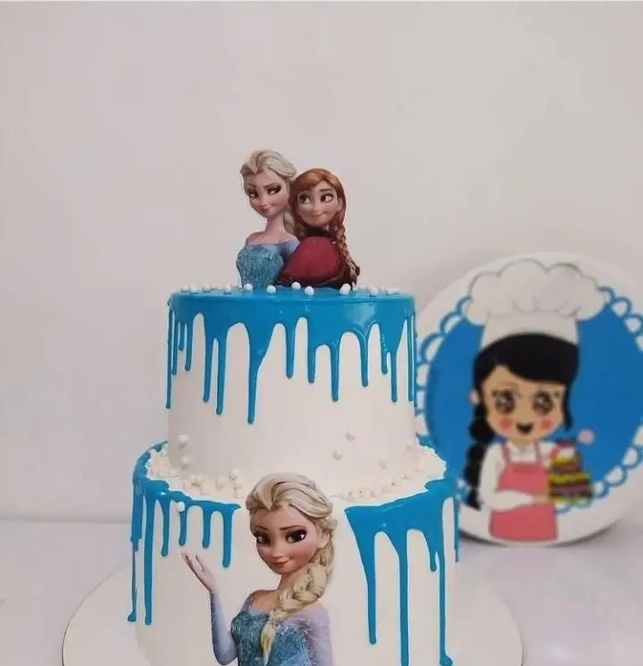 کیک تولد دو طبقه تم فروزن با تاپر السا و آنا، دریپ آبی و تصویر السا. کیک فانتزی و دخترانه برای سفارش از قنادی سهند.