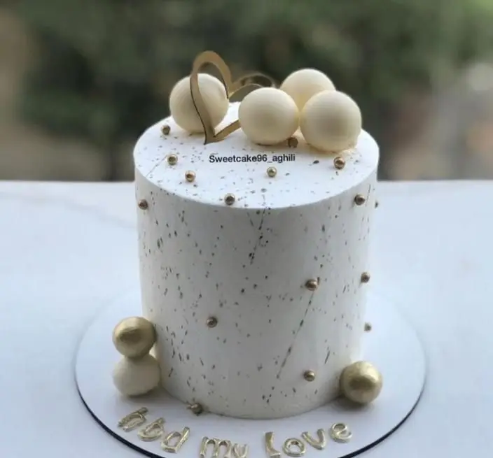 کیک تولد خاص و عاشقانه از قنادی سهند، سفید و طلایی، با تزیینات مروارید، قلب و حروف hbd my Love برای مناسبت های ویژه.