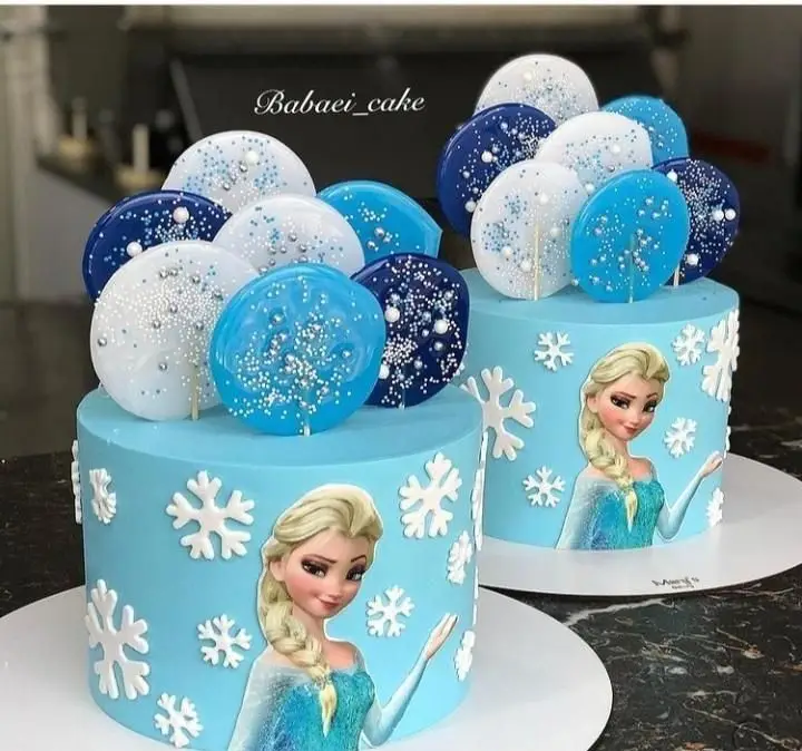 دو کیک تولد دخترانه فروزن السا از قنادی سهند، با خامه آبی، دانه های برف سفید، و آبنبات های دایره ای آبی و سفید نقره ای.