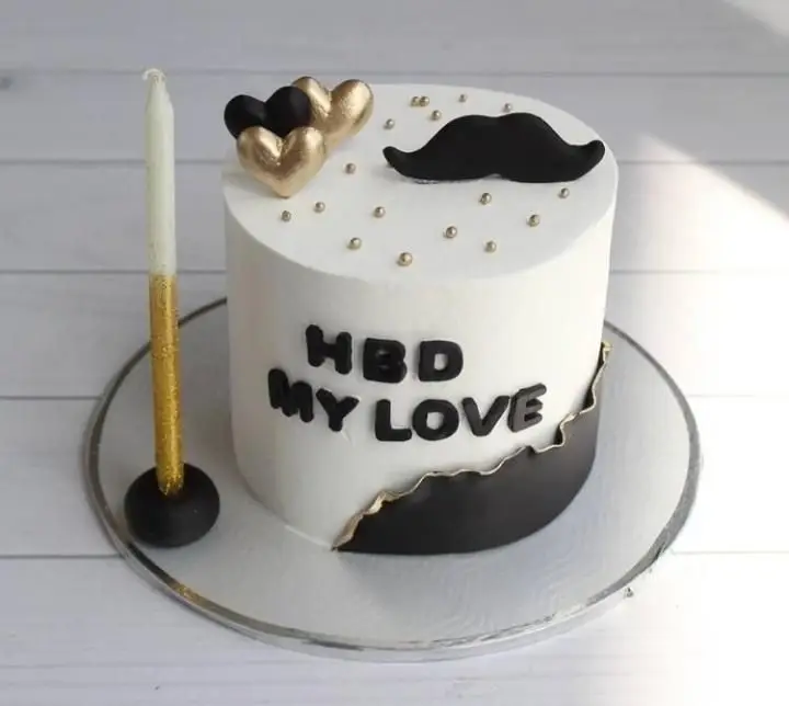 کیک تولد مردانه شیک قنادی سهند با تم مشکی طلایی، تزیین سبیل و قلب‌های طلایی، متن HBD MY LOVE و شمع خاص.