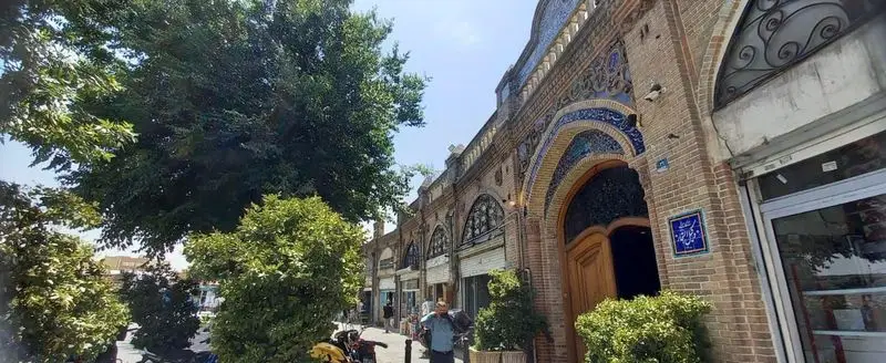 نمای زیبا از کافه رستوران وکیل التجار با معماری سنتی آجری، کاشی‌کاری آبی، و فضای دلنشین در خیابانی سرسبز و تاریخی.