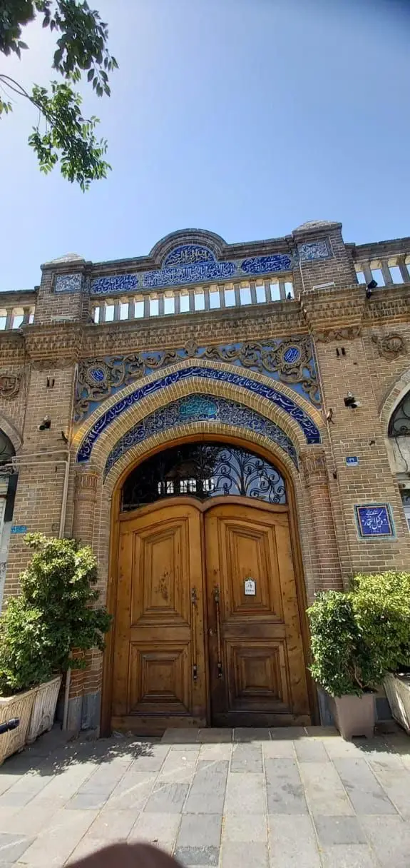 نمای زیبای کافه رستوران وکیل التجار با درب چوبی سنتی، کاشی‌کاری آبی و خطاطی ایرانی بر سردر ورودی، جلوه‌ای دلنشین و تاریخی.
