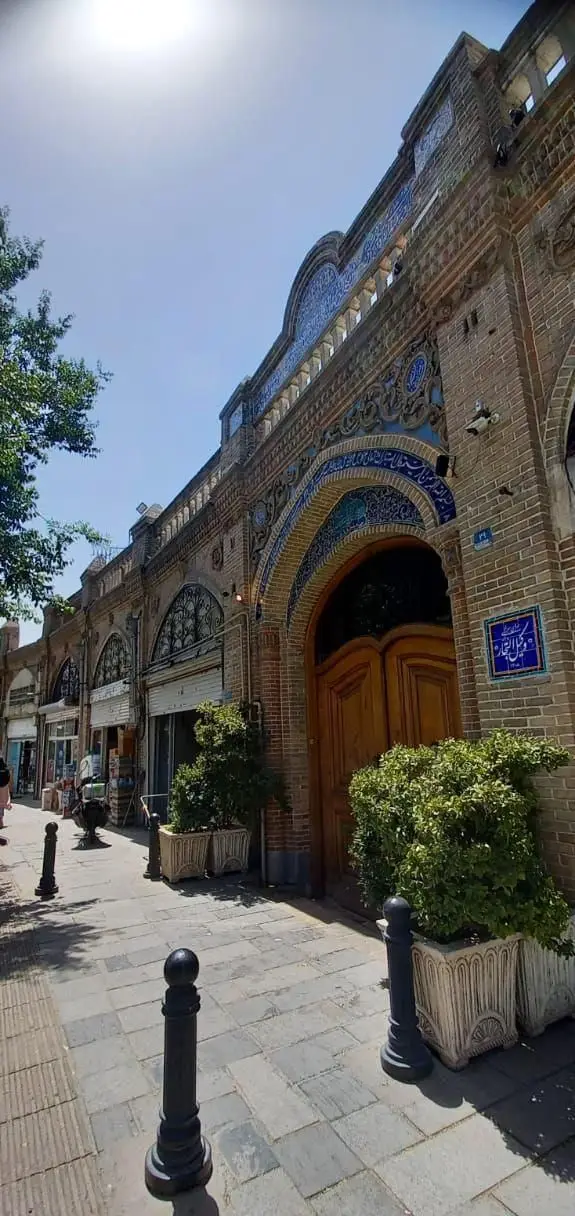 نمای زیبای کافه رستوران وکیل التجار با معماری سنتی ایرانی، کاشی‌کاری آبی خیره‌کننده و ورودی چوبی بزرگ در یک روز آفتابی.
