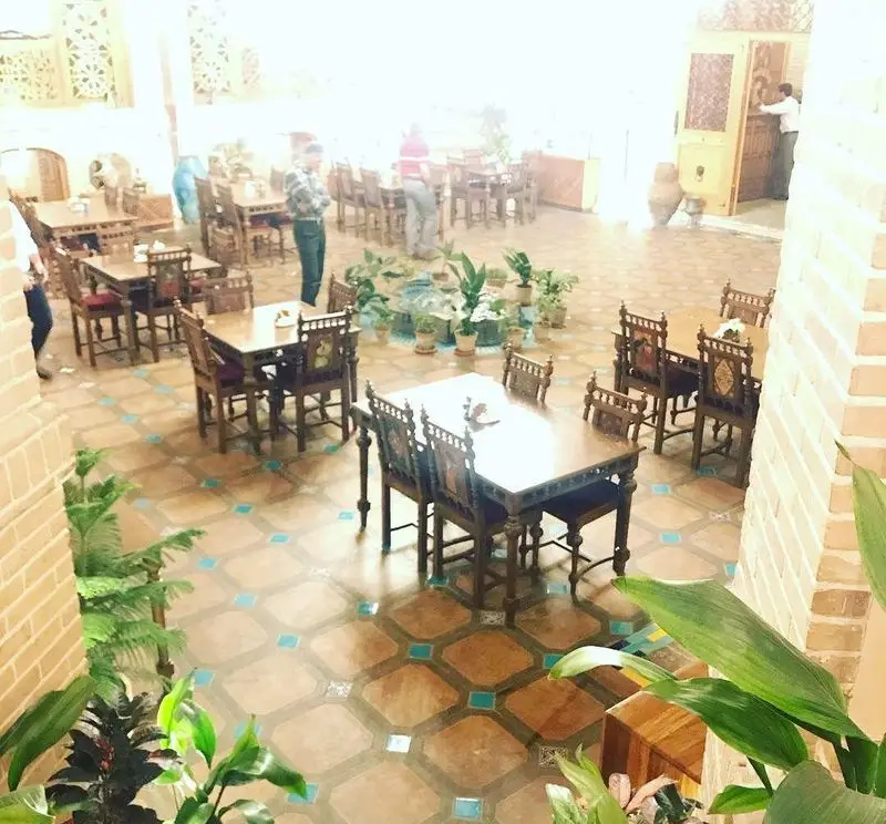 فضای داخلی کافه رستوران وکیل التجار، با معماری و دکوراسیون سنتی ایرانی، میز و صندلی‌های چوبی و گلدان‌های طبیعی.