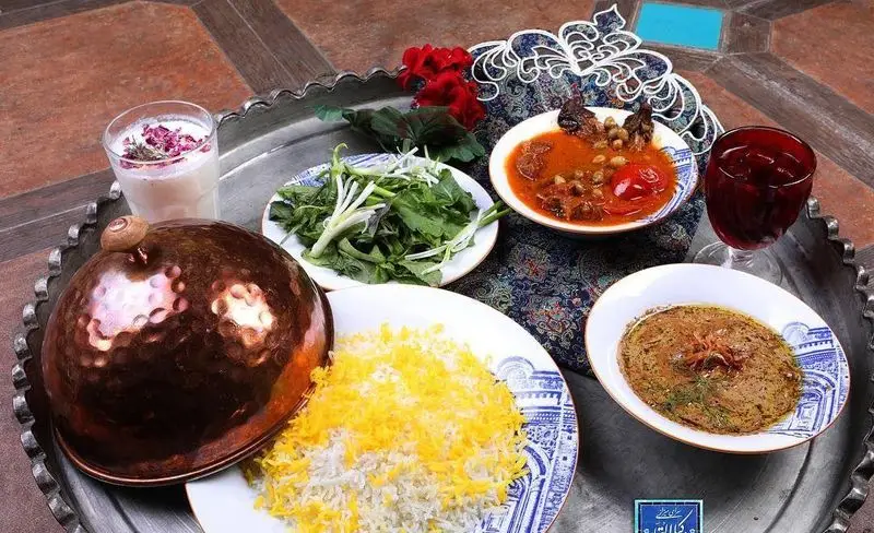سفره رنگین کافه رستوران وکیل التجار با انواع غذای سنتی ایرانی شامل برنج زعفرانی، خورش، پیش‌غذا، سبزی و دوغ محلی.