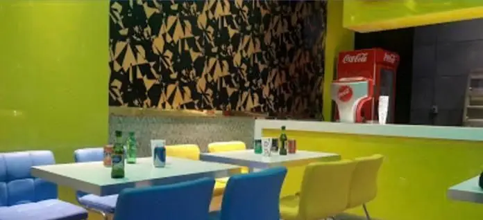 فضای داخلی فست فود لیانو با دکوراسیون شیک و مدرن، دیوارهای سبز لیمویی، طرح دیواری خاص و میز و صندلی‌های آبی و زرد.