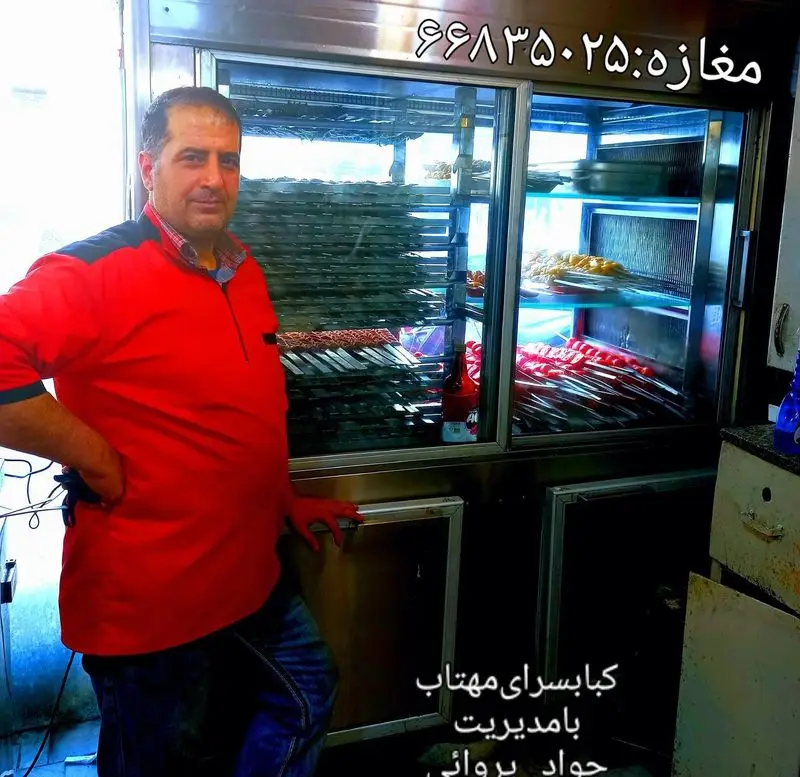 تصویر جواد پروائی، مدیر کباب سرای مهتاب جاسبی، با ویترین پر از انواع کباب‌های تازه و خوشمزه.