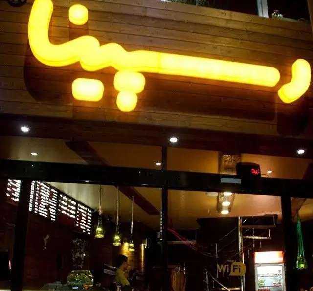 تابلوی نئون درخشان و زرد رنگ فست فود رسپینا در نمای بیرونی رستوران، جذابیت دکوراسیون داخلی مدرن را از ورودی نشان می‌دهد.