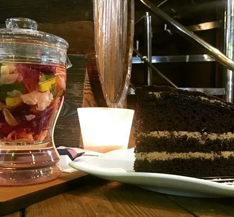 برش کیک شکلاتی رسپینا با لایه‌های کرم، نوشیدنی دتاکس میوه‌ای تازه و شمع روشن در محیط دلنشین فست فود رسپینا.