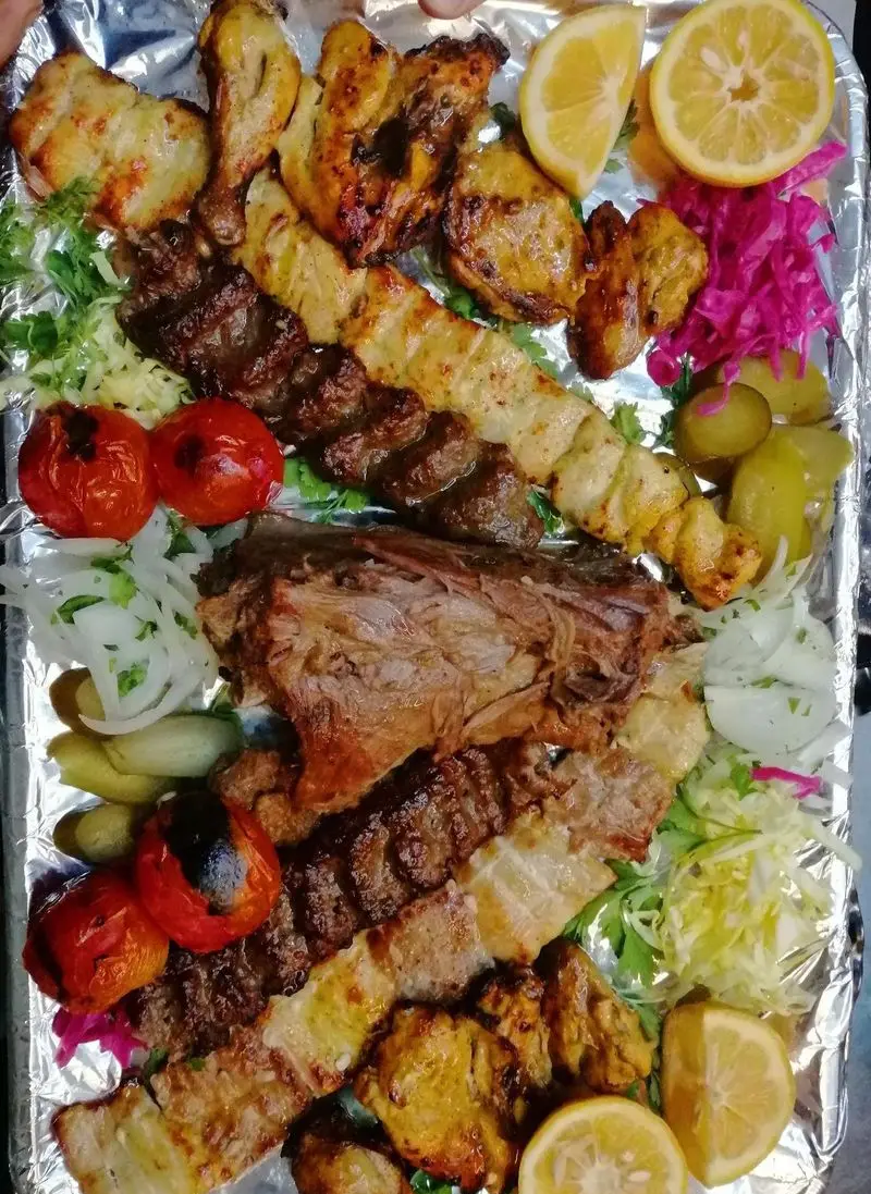 سینی بزرگ و اشتهاآور باغ رستوران ریحانه با انواع کباب‌های گوشت و مرغ، جوجه کباب لذیذ، گوشت بره تنوری، گوجه و پیاز کبابی و لیموترش تازه.