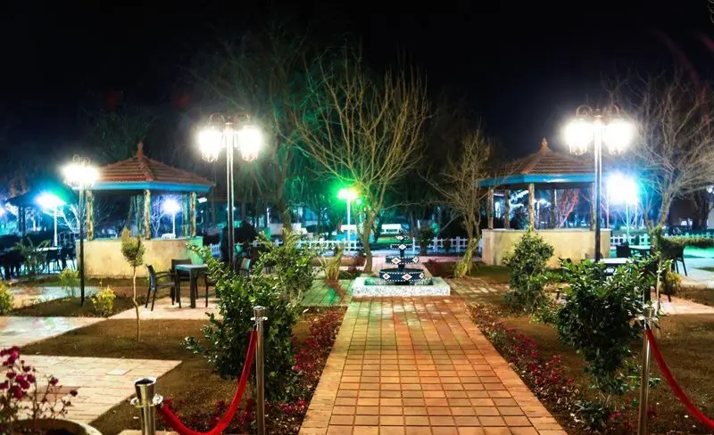 نمای شب باغ رستوران ریحانه با نورپردازی دلنشین، آلاچیق‌های زیبا و فضای باز رمانتیک، مناسب برای دورهمی‌های شبانه در محیطی آرام.