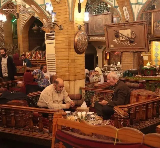 محیط گرم و سنتی سفره خانه باغ صبا، با میهمانانی که در تخت‌های سنتی نشسته و از فضای دلنشین و دکوراسیون ایرانی لذت می‌برند.