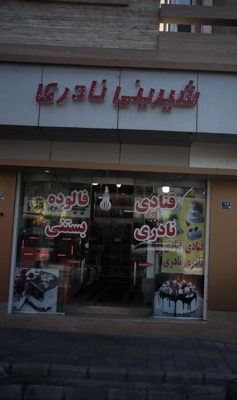 نمای بیرونی مغازه شیرینی نادری با تابلوهای قنادی نادری و فالوده بستنی، همراه با عکس های انواع کیک و شیرینی های خوشمزه.