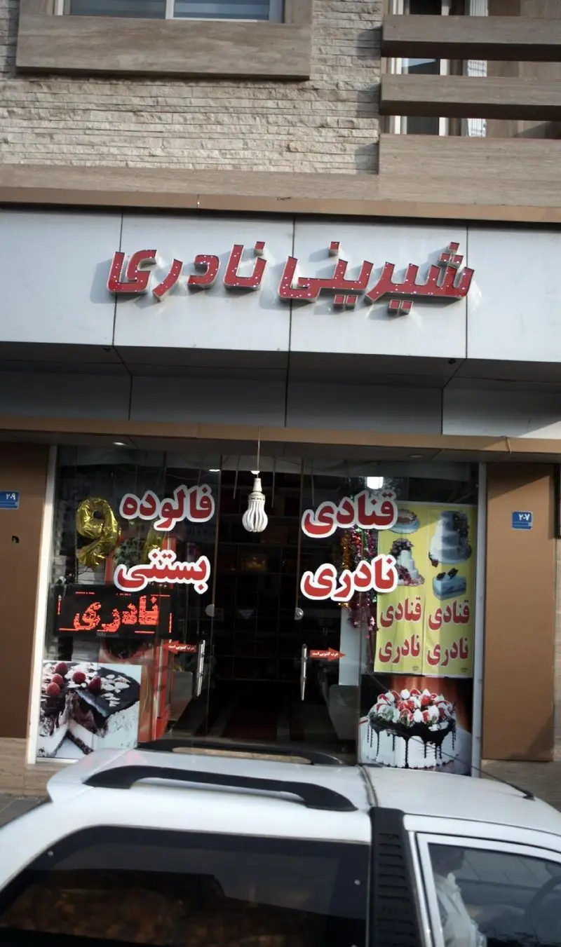 نمای بیرونی قنادی و شیرینی‌فروشی نادری به همراه تابلو و ویترین شامل انواع کیک، شیرینی، فالوده و بستنی