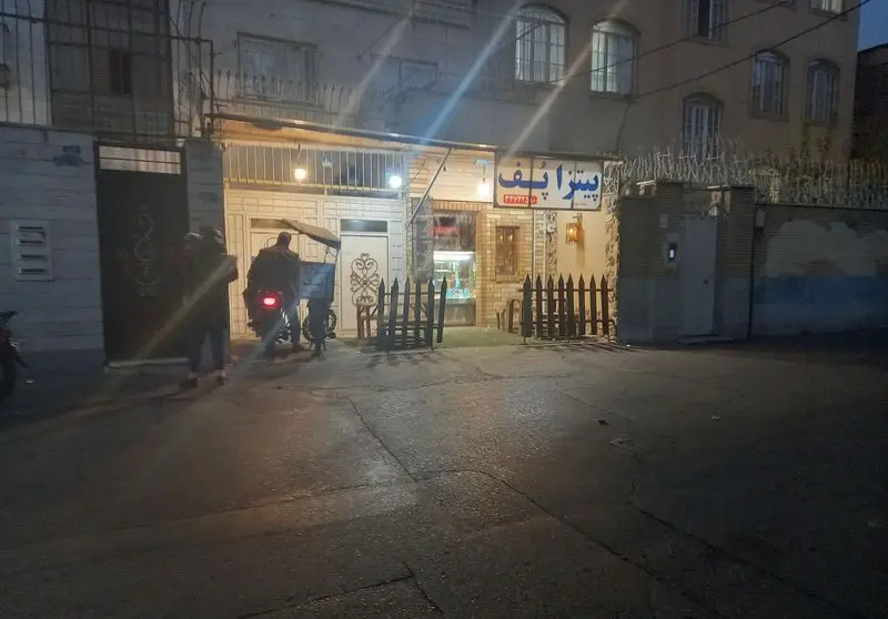 تصویر شب از ورودی فست فود پیتزا پف با تابلوی درخشان، حضور پیک موتوری برای ارسال سفارشات پیتزا و فست فود در محله