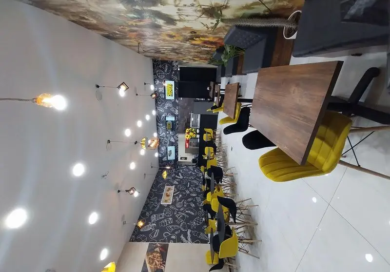 فضای داخلی فست فود آفتابگردان با دکوراسیون مدرن، میز و صندلی‌های زرد و مشکی. دیوارنگاری غذایی جذاب و سقف با طرح آفتابگردان. نورپردازی دلنشین و محیطی آرام.