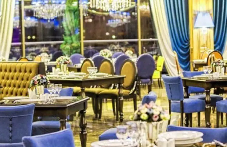 فضای داخلی لوکس کافی شاپ کاخ لیدوما با میزهای چیده شده، صندلی‌های شیک آبی و طلایی و چشم‌انداز شهری دلنشین برای صرف غذا.