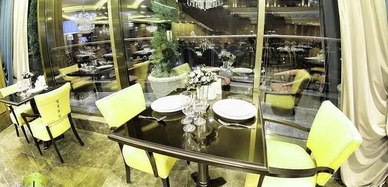 دکوراسیون داخلی کافی شاپ کاخ لیدوما با میزهای چیده شده، صندلی‌های لیمویی و پنجره‌های بلند، فضایی شیک و آرامش‌بخش را نشان می‌دهد.