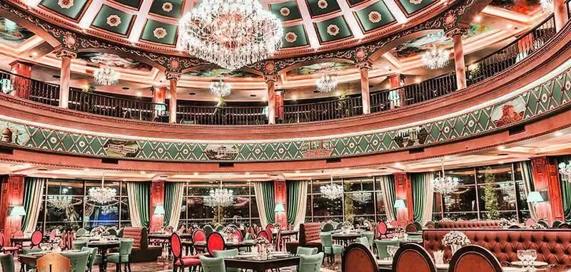 فضای داخلی لوکس و زیبای کافی شاپ کاخ لیدوما با دکوراسیون باشکوه، لوسترهای کریستالی و میز و صندلی‌های چیده شده.