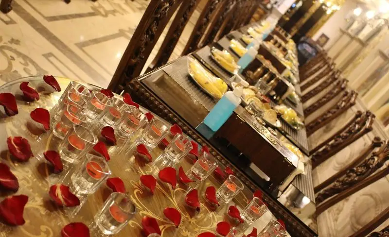 فضای مجلل کاخ رستوران نقش جهان با میز بوفه شیک، شامل دسرها، میوه‌ها، گلبرگ رز و تزیینات رمانتیک برای مراسم خاص.