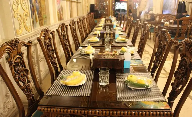 تصویری از داخل کاخ رستوران نقش جهان: میز غذاخوری مجلل با صندلی‌های منبت‌کاری شده چوبی و میوه‌های آماده پذیرایی.