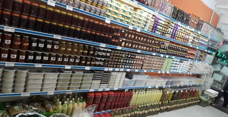 قفسه‌های پر از محصولات لبنی، عسل، مربا، ادویه و ترشیجات در فروشگاه لبنیات امیر لیقوانی، نمایشگر تنوع کالاهای تازه و محلی.