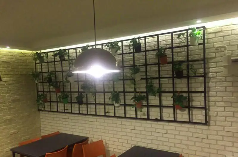 نمایی از فضای داخلی رستوران ایتالیایی بولونیز با دیوارهای آجری سفید و زرد، دکوراسیون سبز گیاهان در گلدان روی دیوار و نورپردازی مدرن.