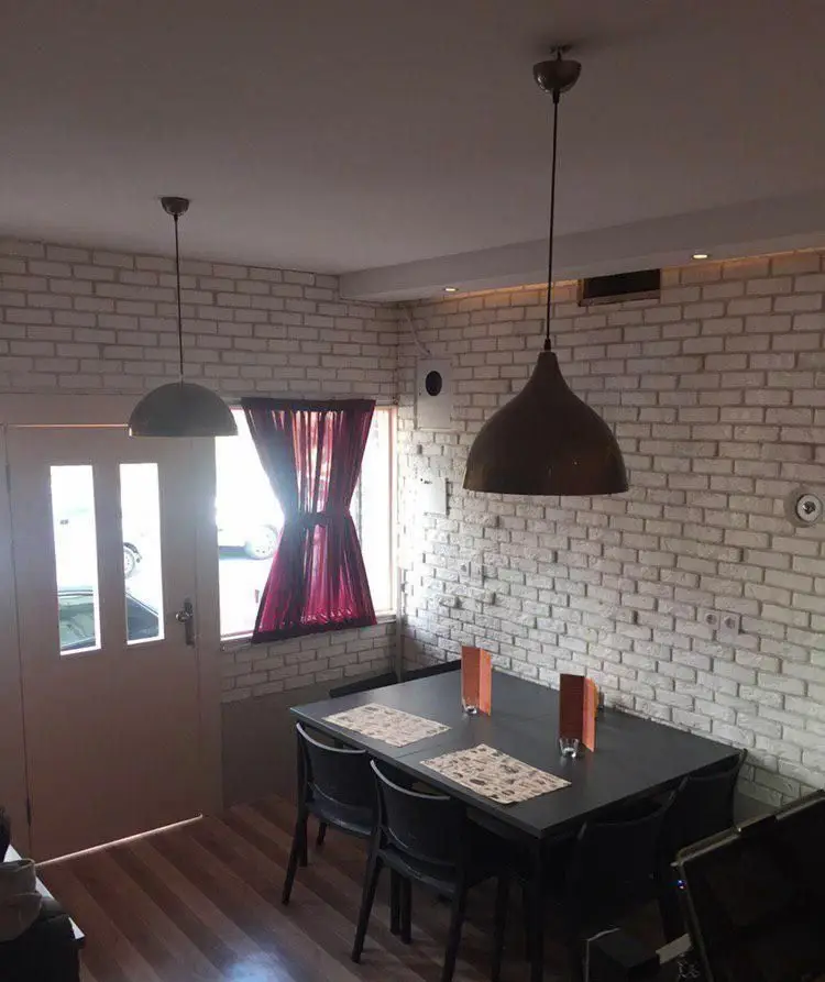 فضای داخلی جذاب رستوران ایتالیایی بولونیز با دیوارهای آجری سفید، میز و صندلی‌های شیک، چراغ‌های آویز مدرن و پرده قرمز.