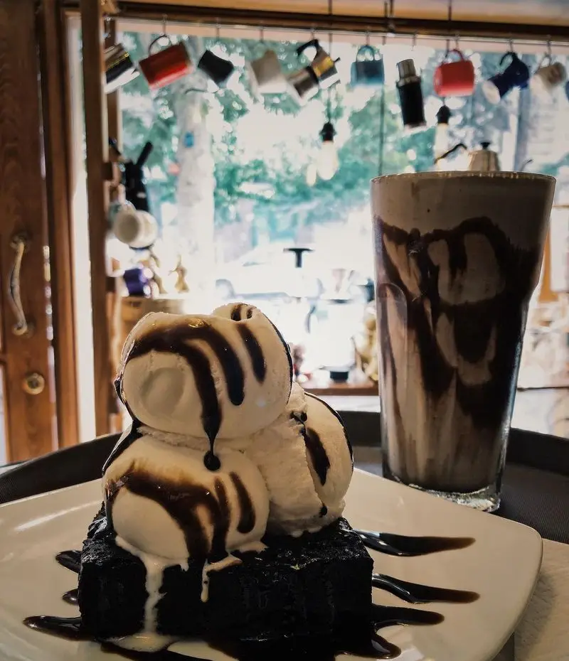 دسر براونی شکلاتی با بستنی وانیلی و سس غلیظ، در کنار میلک شیک در کافه ایستگاه لاله. تجربه طعم شیرین و خنک در فضایی دلنشین.