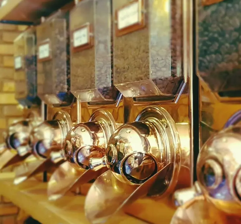 دستگاه های دیسپنسر طلایی رنگ دانه های قهوه تازه و باکیفیت در کافه ایستگاه لاله، تجربه ای لذت بخش از انتخاب قهوه.