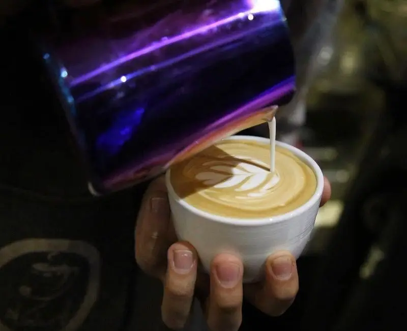 باریستا ماهر در کافه ایستگاه (لاله) در حال ساخت یک لاته آرت چشم‌نواز با شیر بخار داده شده روی قهوه تازه. لذت قهوه در لاله.