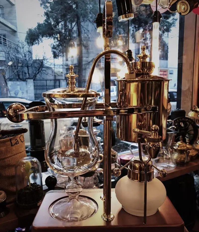 دستگاه قهوه ساز سایفون برنجی و شیشه‌ای با طراحی وینتیج و خاص. تجهیزات حرفه‌ای قهوه در فضای دلنشین کافه ایستگاه لاله تهران.